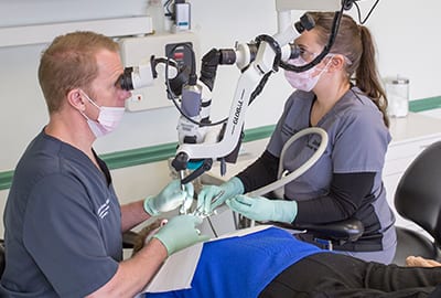 Dr Cross and staff member looking through microscope at patient on table   j David cross dds